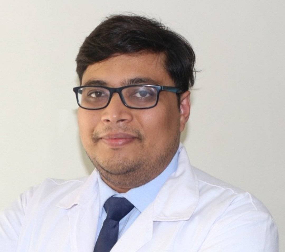 A male doctor with glasses wearing a white coat and blue tie, smiling at the camera.